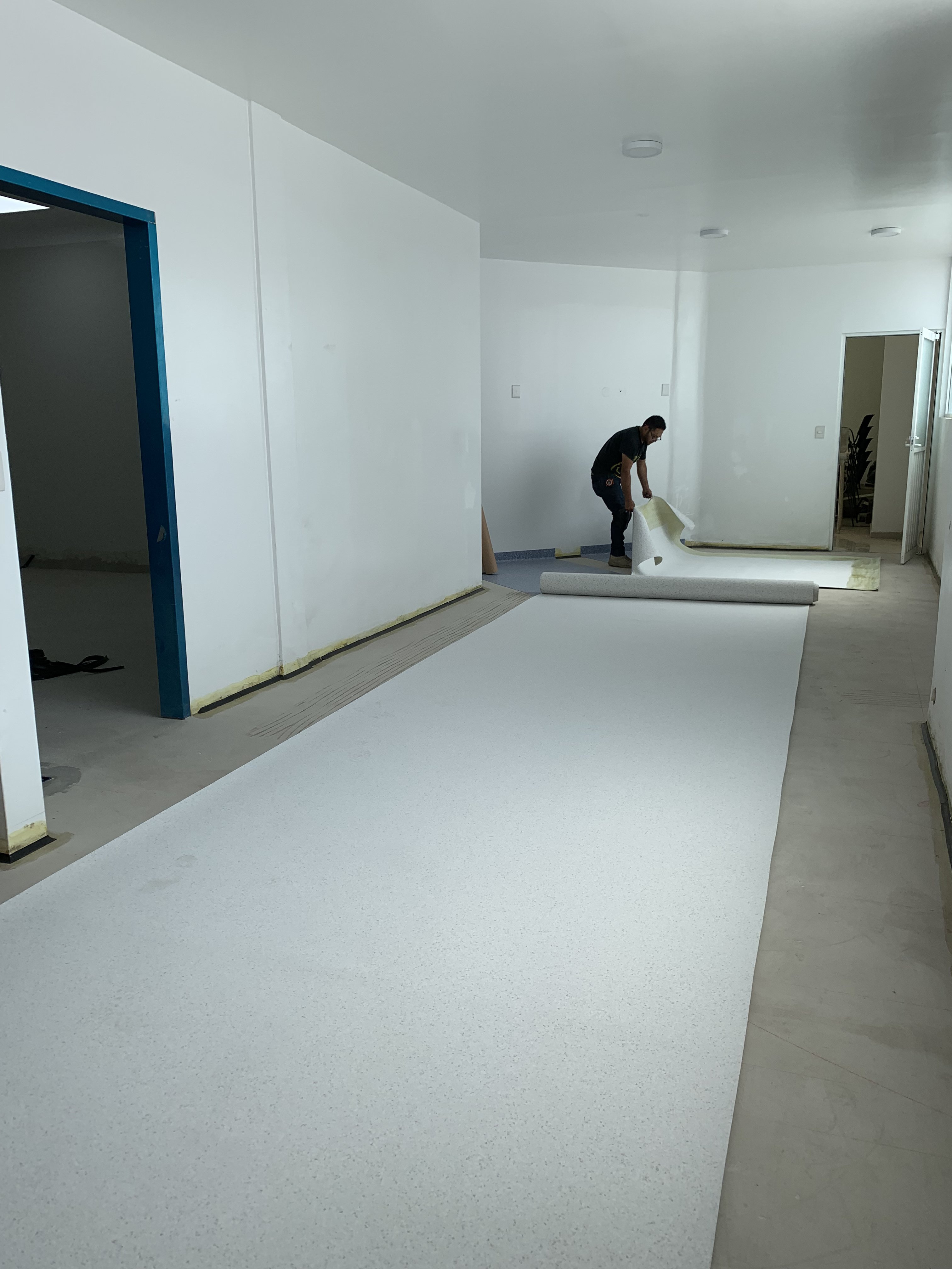 Técnico desenrollando piso homogéneo en pasillo clínico